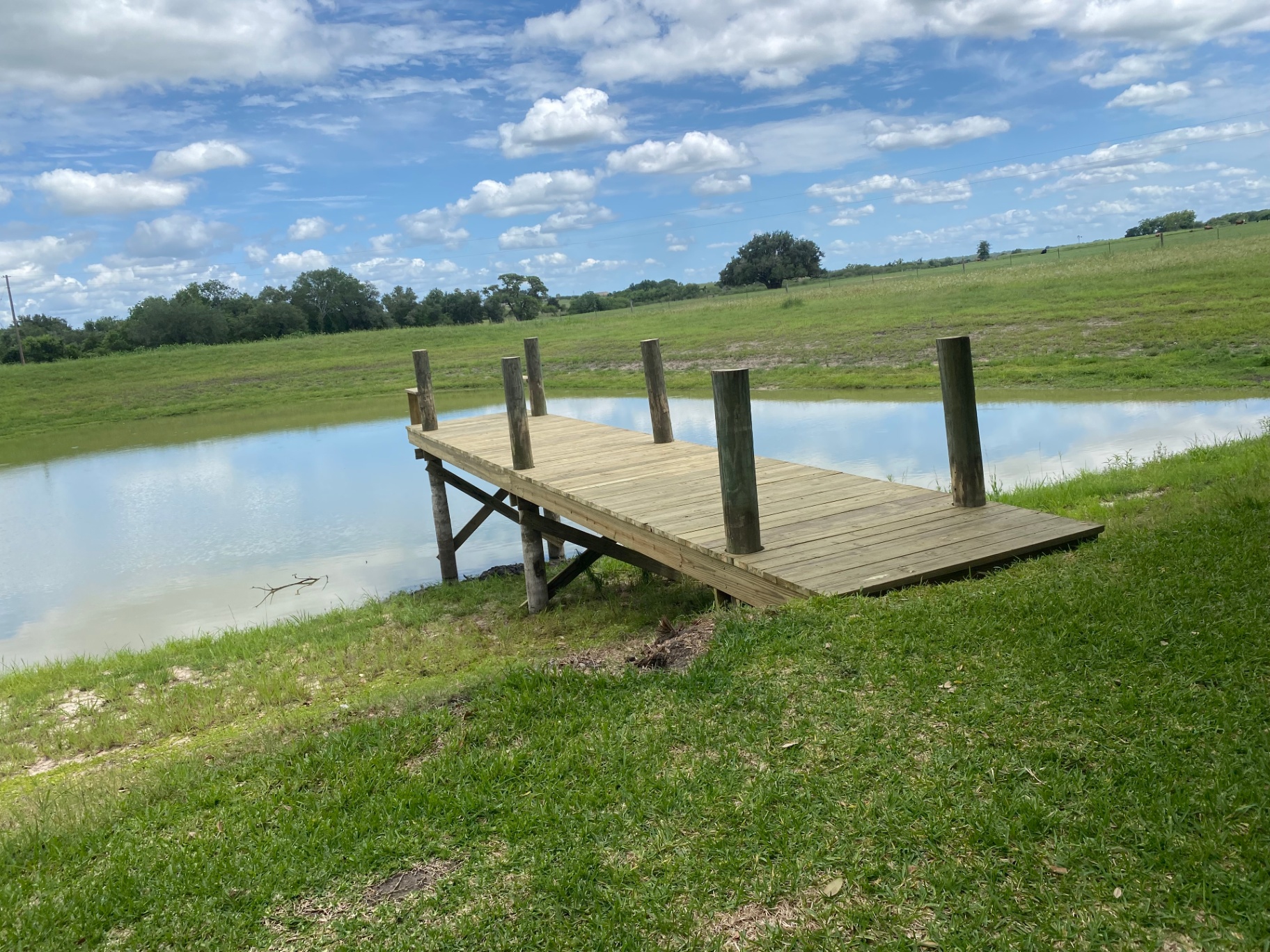 Custom wood pond dock with pilings extending over a rural Texas pond