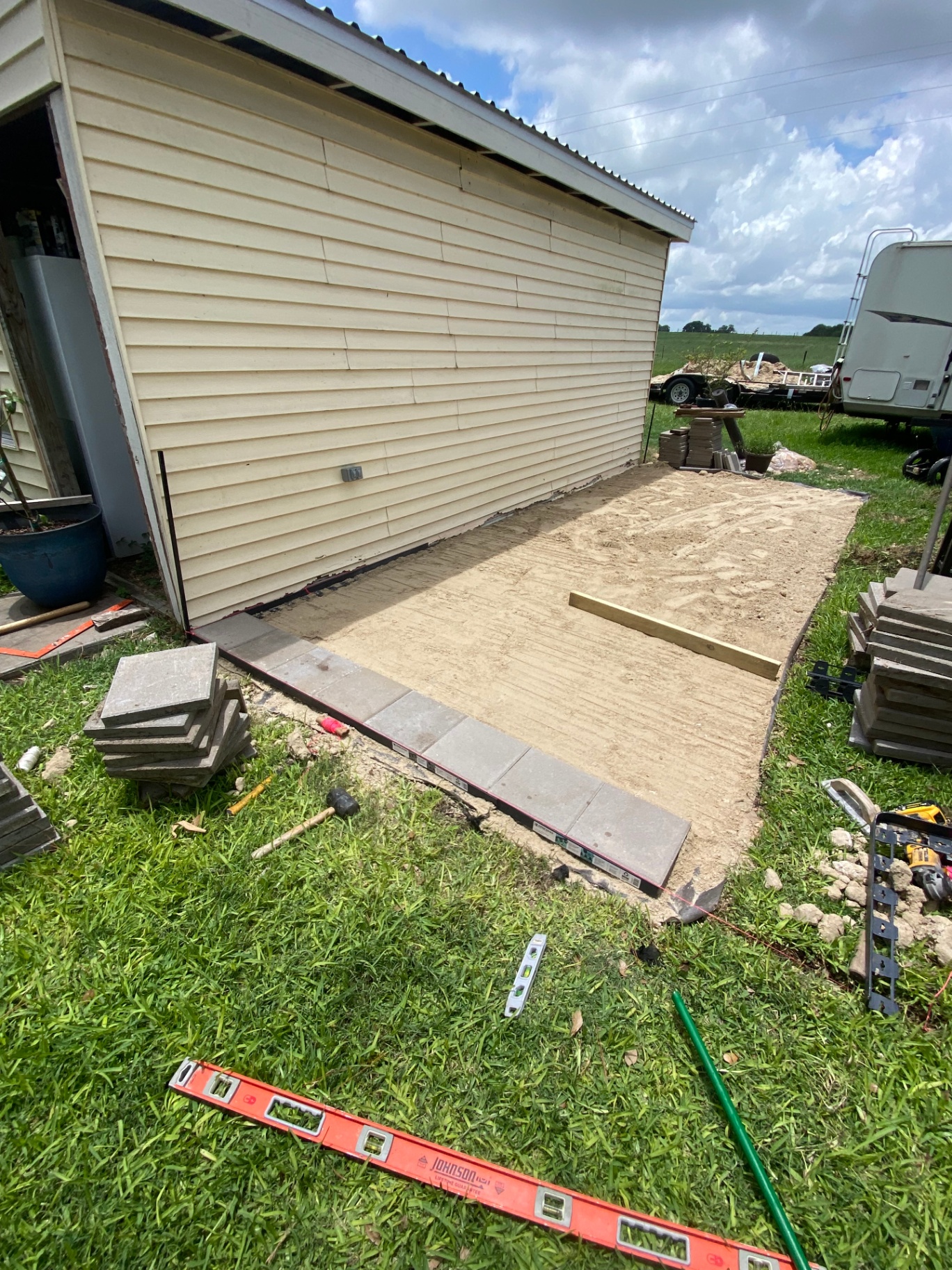Paver patio layout and base prep underway beside an outbuilding