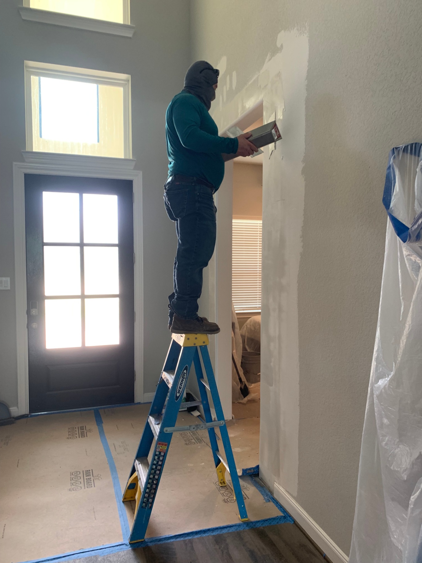 Old School Construction crew member painting a high interior wall from a ladder