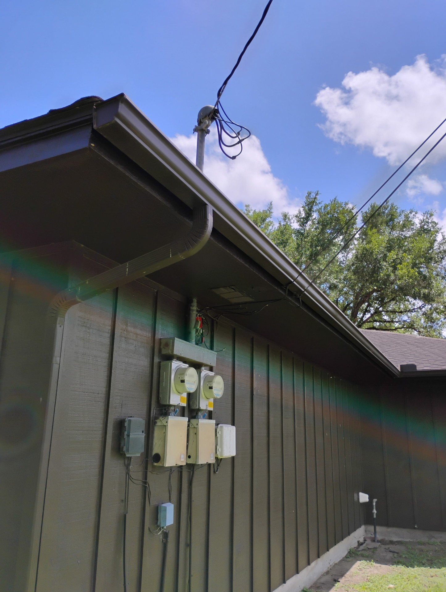 New brown seamless gutters installed on dark green board-and-batten siding