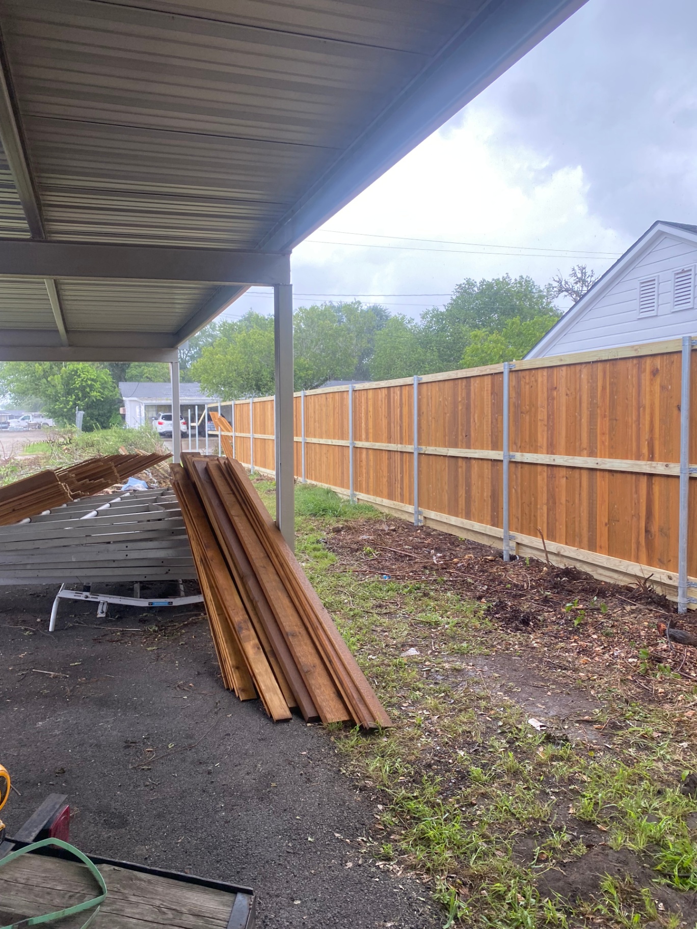 Long cedar privacy fence installation running behind a covered parking area