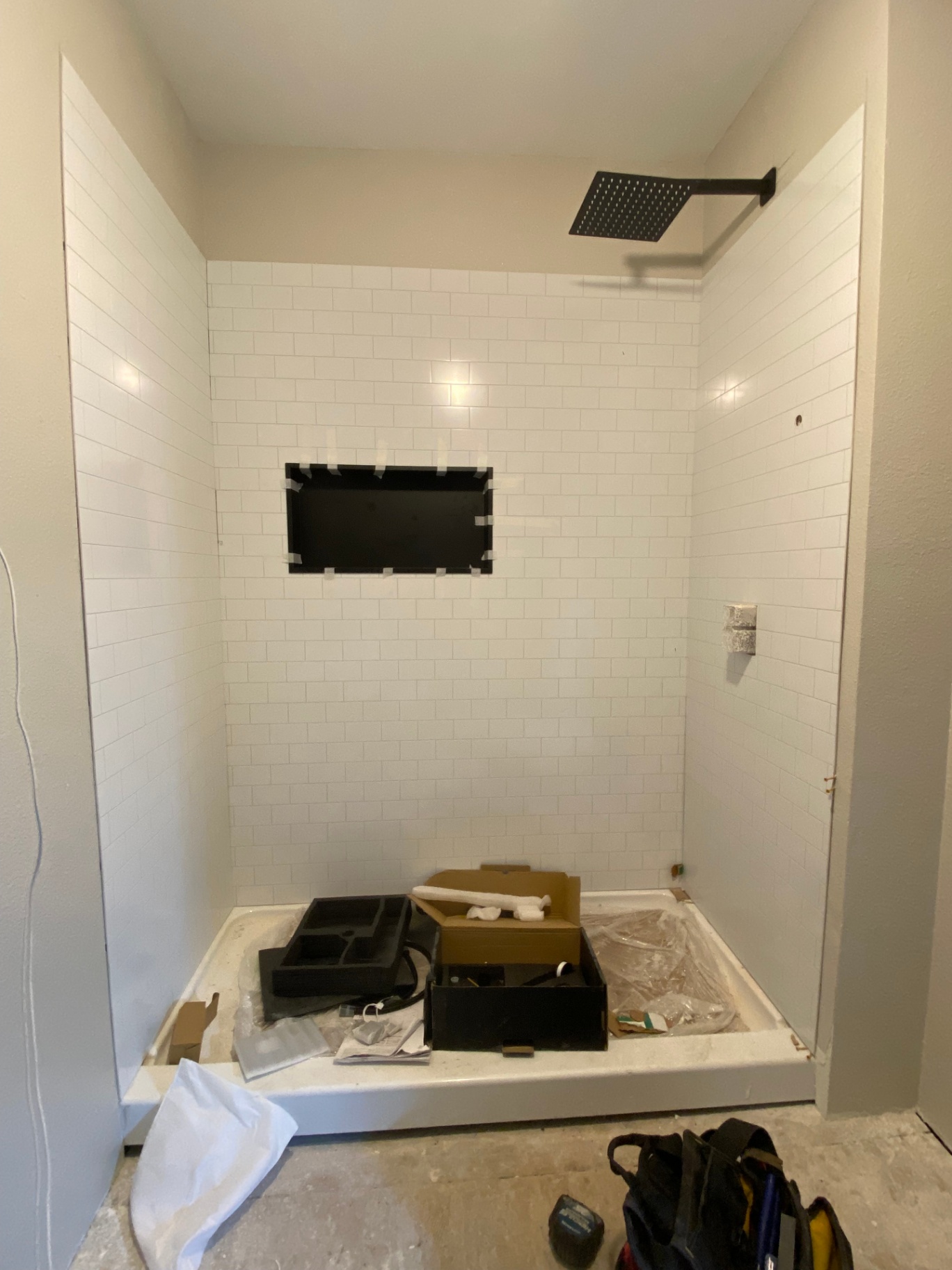 Walk-in shower tile installation in progress with white subway tile and black niche
