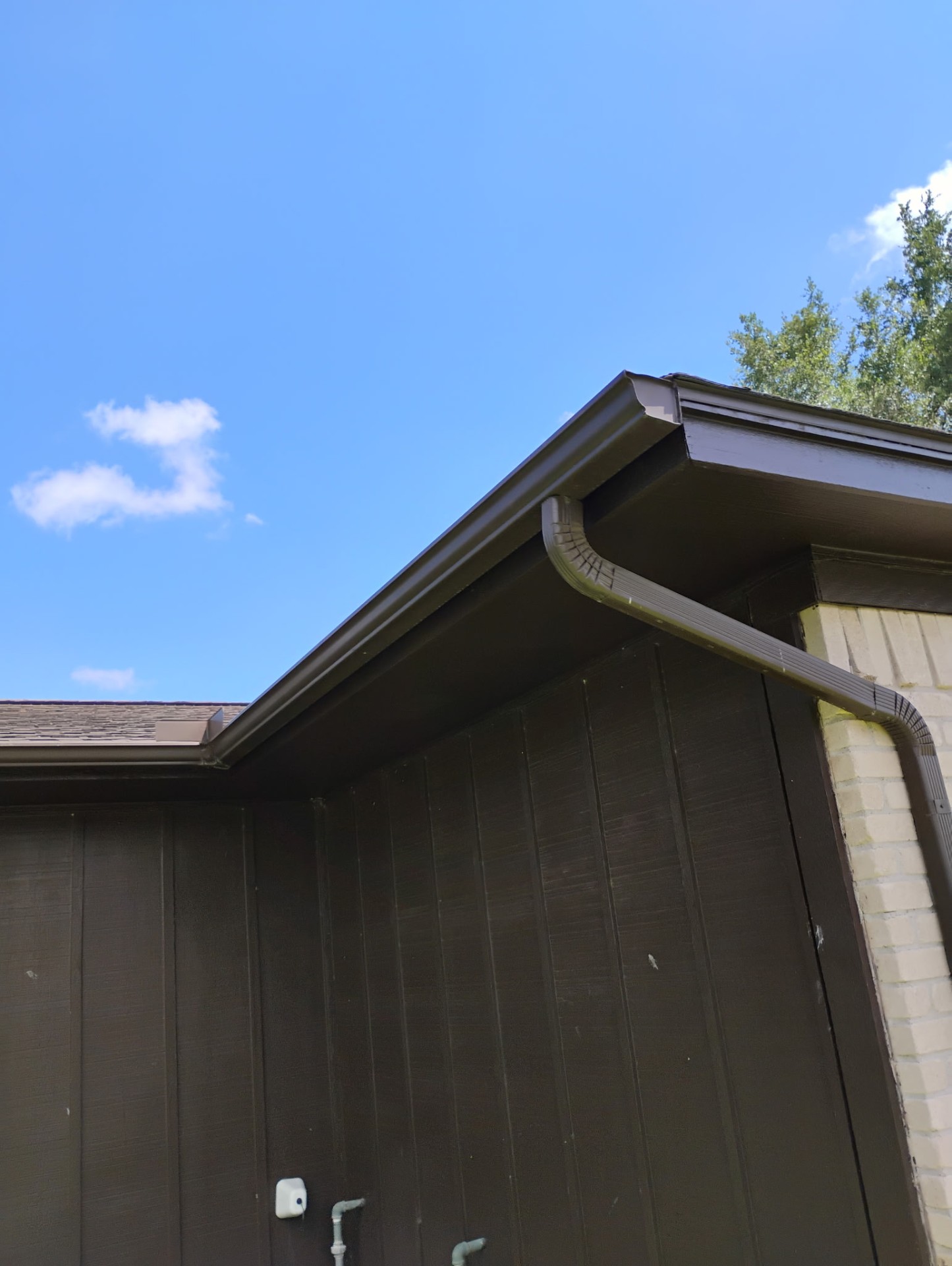 Brown gutter and downspout installed on a Texas home's brick corner