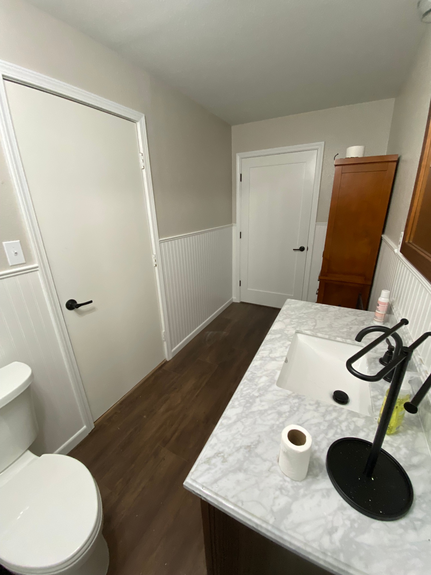 Finished bathroom vanity with marble-look countertop, black fixtures, and beadboard walls